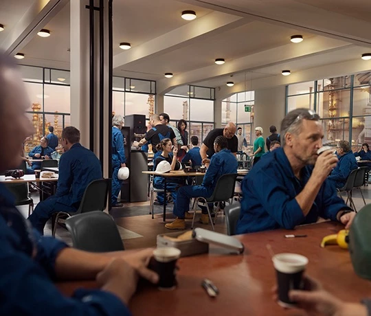 Mehrere Arbeiter sitzen an Tischen oder bedienen sich von der Jacobs Professional Cafitesse Quantum 120 Kaffeemaschine.