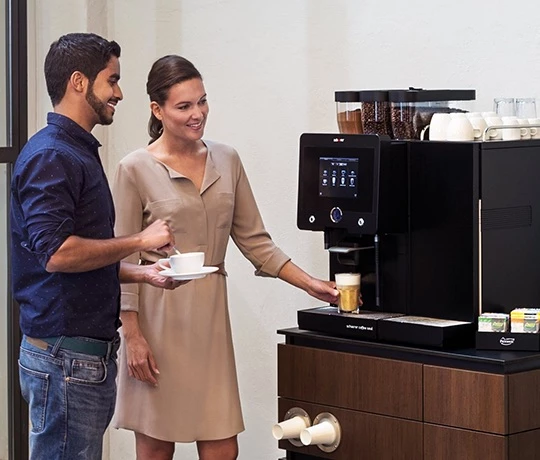 Eine Frau und ein Mann holen sich gerade Kaffee von einem Jacobs Professional Schaerer Coffee Soul Kaffeevollautomat.