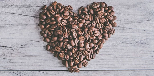 Kaffeebohnen sind auf einem Holztisch in der Form eines Herzens gelegt.