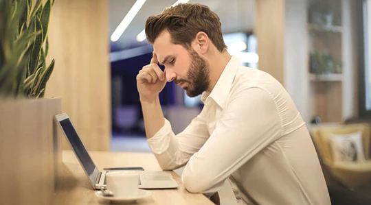 Abbildung eines Mannes mit Kopfschmerzen und einer Tasse Kaffee.