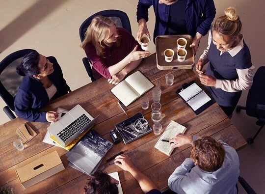 Eine Gruppe Mitarbeiter sitzt im Büro an einem Tisch und bekommt gerade Kaffee serviert.