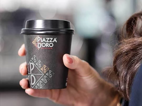 Ein Kaffee-To-Go-Becher von Piazza D'Oro wird gehalten.