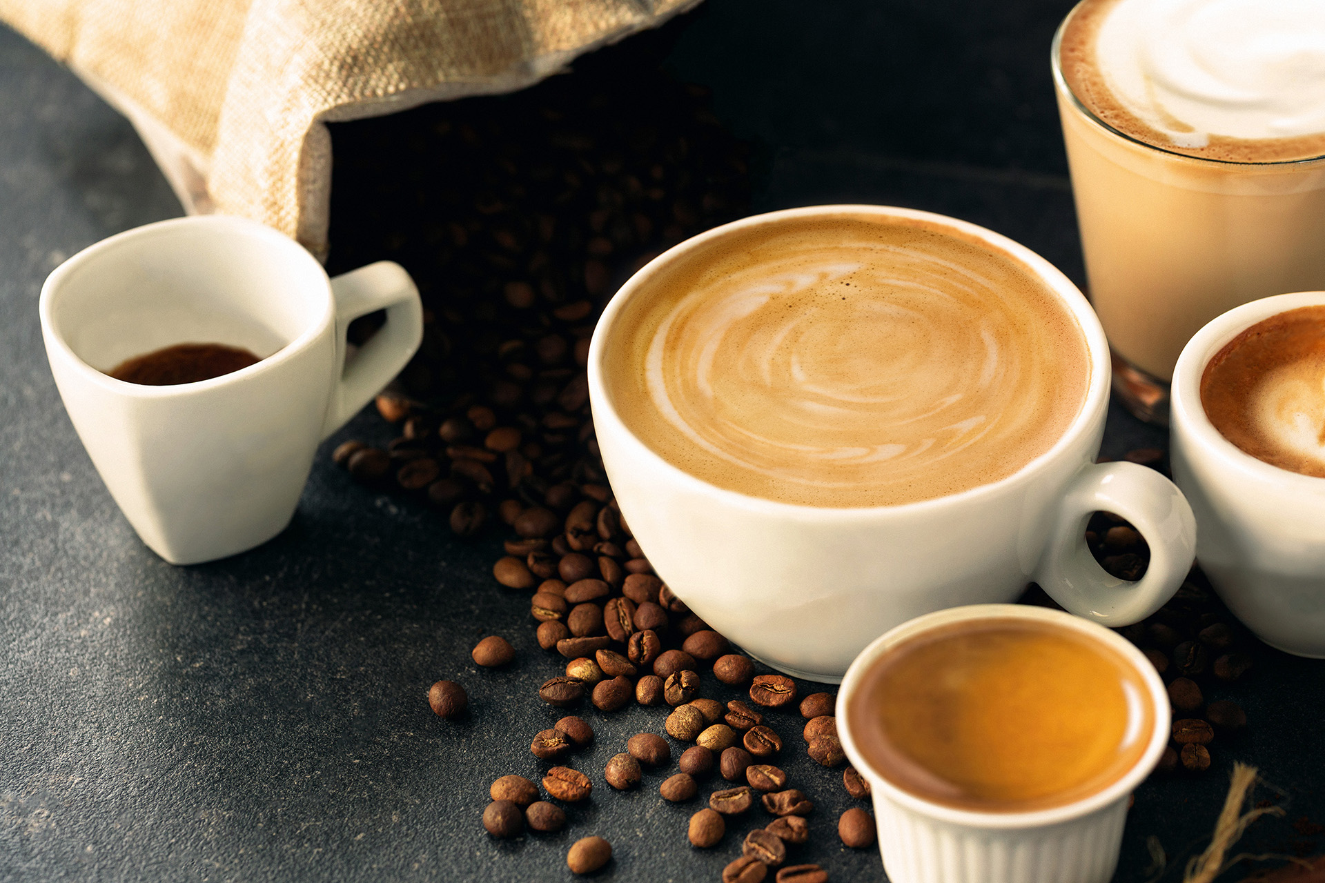 5 Cups of Coffee with different sizes on a tabletop with spilled coffee beans around them