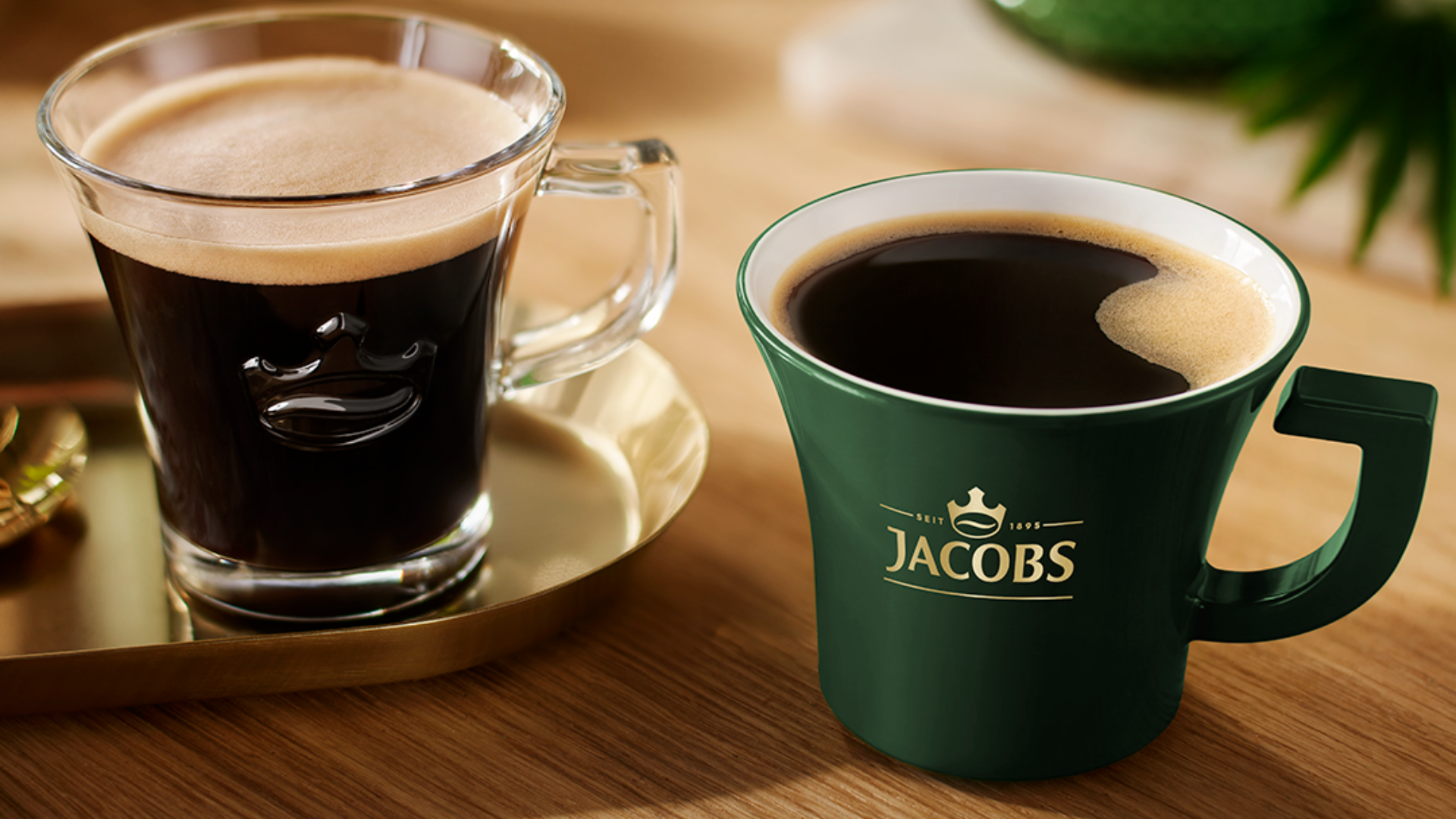Grüne Kaffeetasse mit Schaumkrone neben einem Schachbrett, Logo ‚JACOBS-BREM‘ mit Krone sichtbar.
