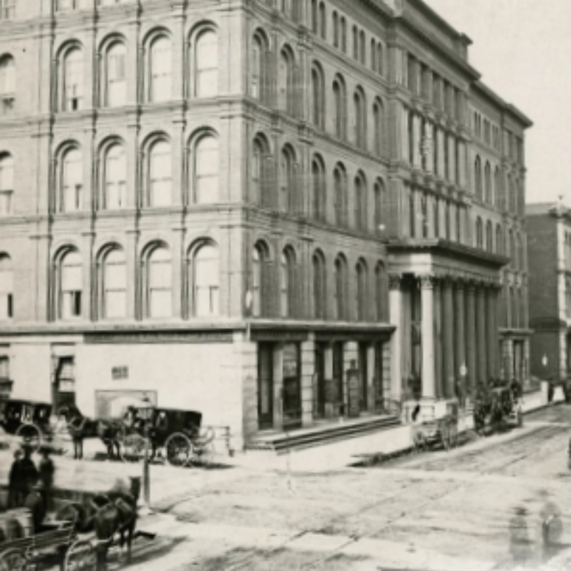 Historische Straßenszene mit klassischem Gebäude, Pferdekutschen und Fußgängern auf einem unbefestigten Weg.