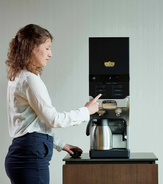 Eine Frau holt sich gerade einen Kaffee an einer Cafitesse Maschine von Jacobs Professional