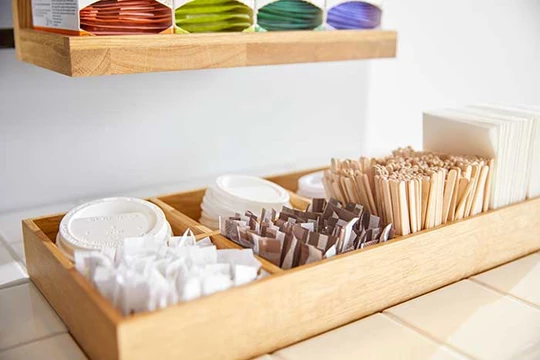 In einer Holzbox sind Zusatzmaterialien für die Kaffeeecke: To Go Becher, Rührstäbe etc.