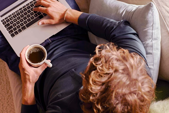 Ein Mann sitzt vor seinem Laptop und trinkt gerade eine Tasse Kaffee von Jacobs Professional