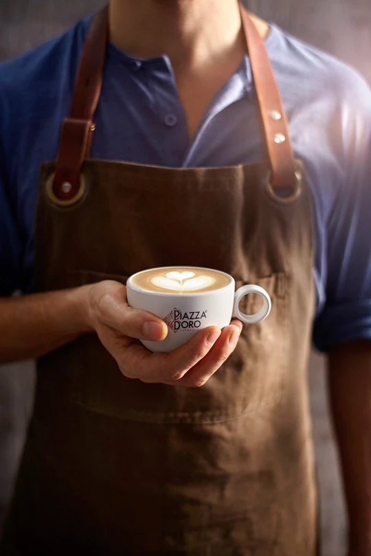 Ein Barista hält eine Tasse Piazza Doro Kaffee in der Hand