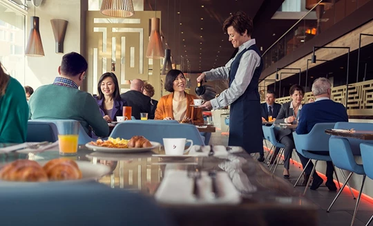 Abbildung einer Bedienung im Cafe, die gerade Jacobs Professional Kaffee serviert.