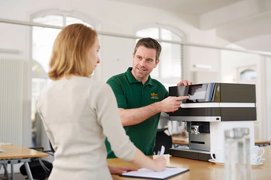 Ein Jacobs Professional Service Mitarbeiter kümmert sich um die Kaffeemaschine einer Kundin.