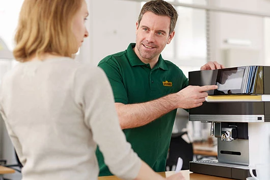 Ein Servicemitarbeiter von Jacobs Professional zeigt einer Kundin die Kaffeemaschine